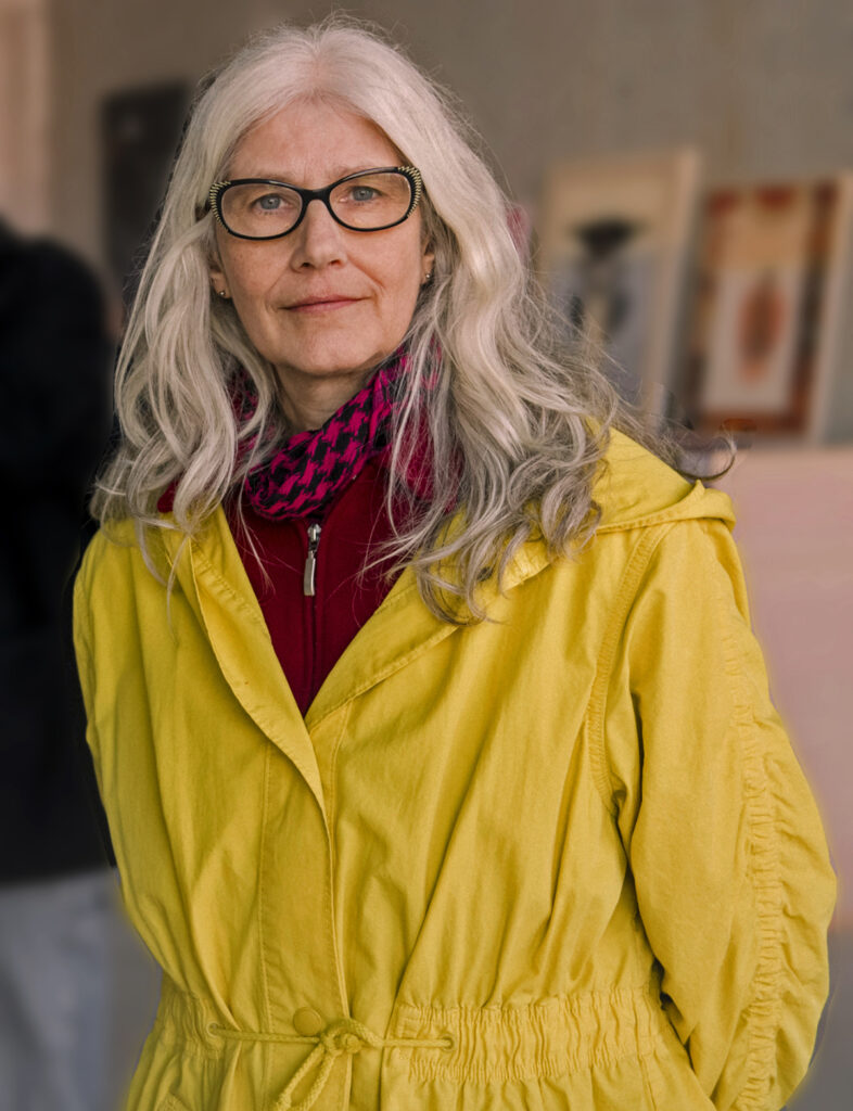 Reggie Voigtländer, kunstenaar en coach bij een expositie, vaag kunstwerken op de achtergrond.